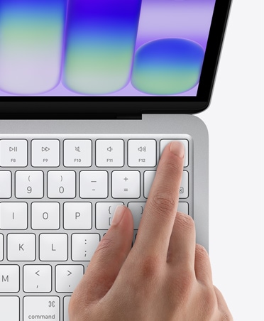 MacBook Neo, silver color, person's finger on Touch ID sensor in top-right corner of keyboard