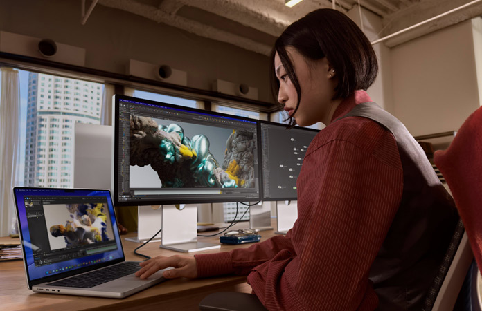 En person sidder i et kontorlandskab med MacBook Pro tilsluttet Studio Display XDR
