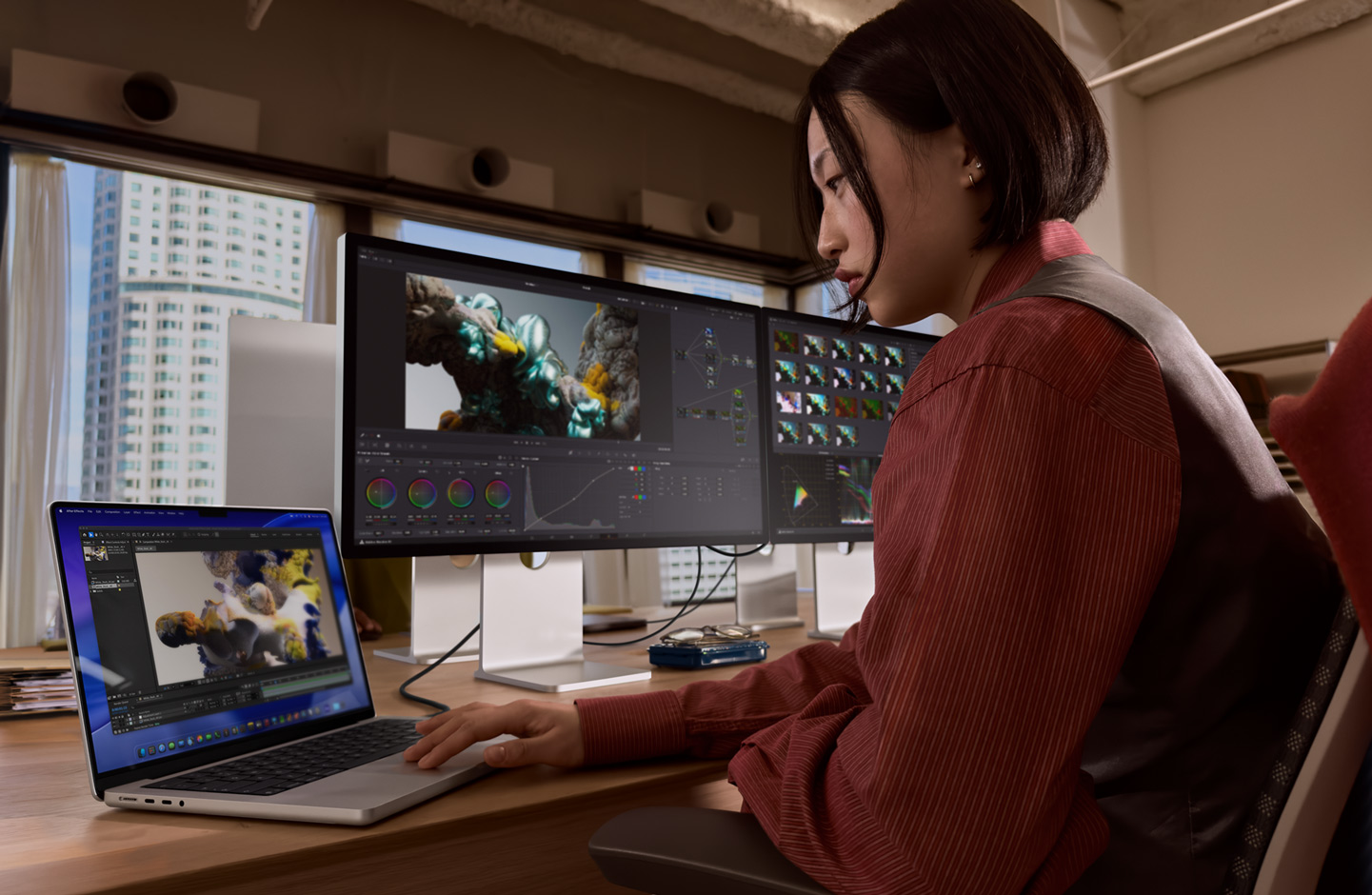 A person in an office setting works on a MacBook laptop that is connected to Studio Display XDR by a Thunderbolt 5 port