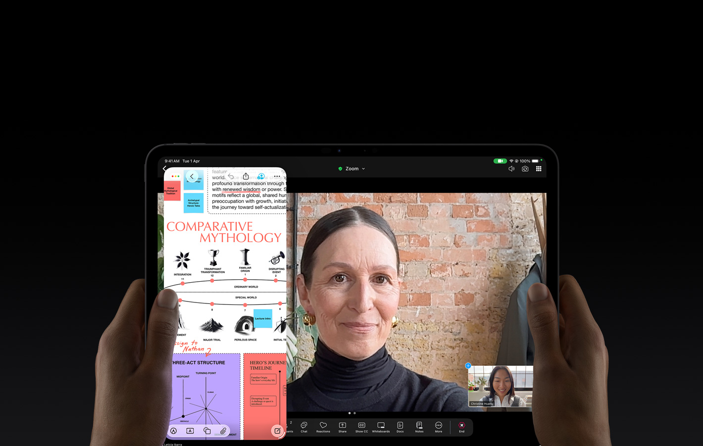 iPad Pro, front exterior, space black color, left and right hands holding in landscape orientation, rounded corners, black display bezel, display showing a FaceTime conversation being live translated, and an educational app showing a presentation of 'Comparative Mythology' with text, diagrams, and handwritten notes