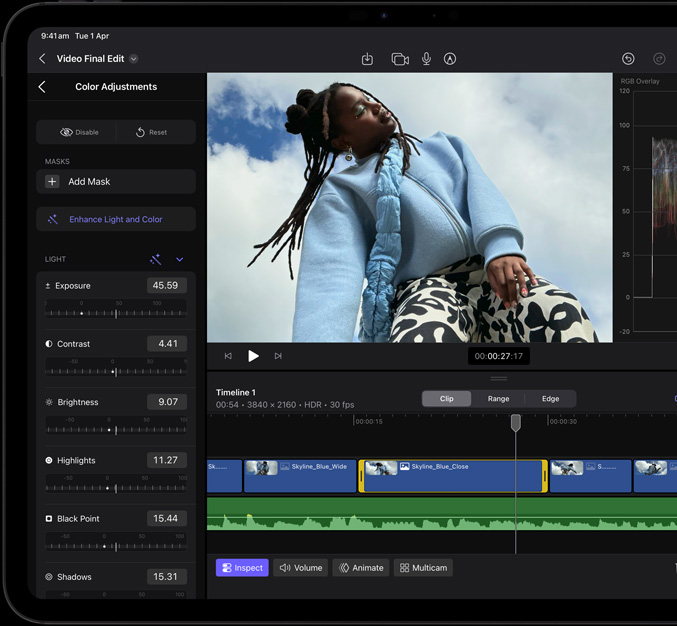 iPad Pro, front exterior, black display bezel, display showing video editing app with a picture of a model in a blue coat and black and white printed pants, colour adjustment panel open on the left with various video effects and sliders, timeline at the bottom with multiple video clips and audio tracks