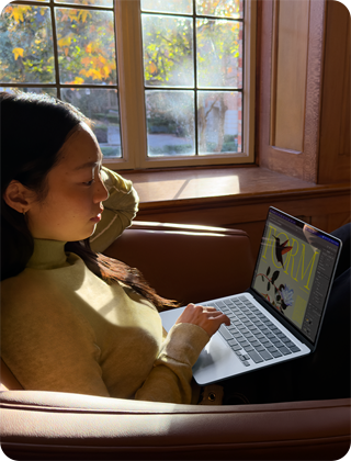 O persoană stă pe un scaun și folosește un MacBook Air