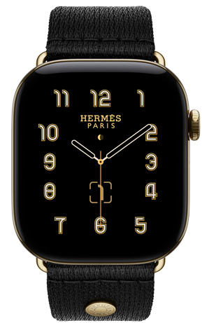 Apple Watch Hermès Series 12, Clou de Selle analogue watch face (hour, minute and second hands, complications: lunar phase, date), titanium case, radiant gold colour, right side exterior, Digital Crown, side button, paired with Noir Satin Clou de Selle band, smooth black satin webbing with radiant gold hardware that matches the watch case