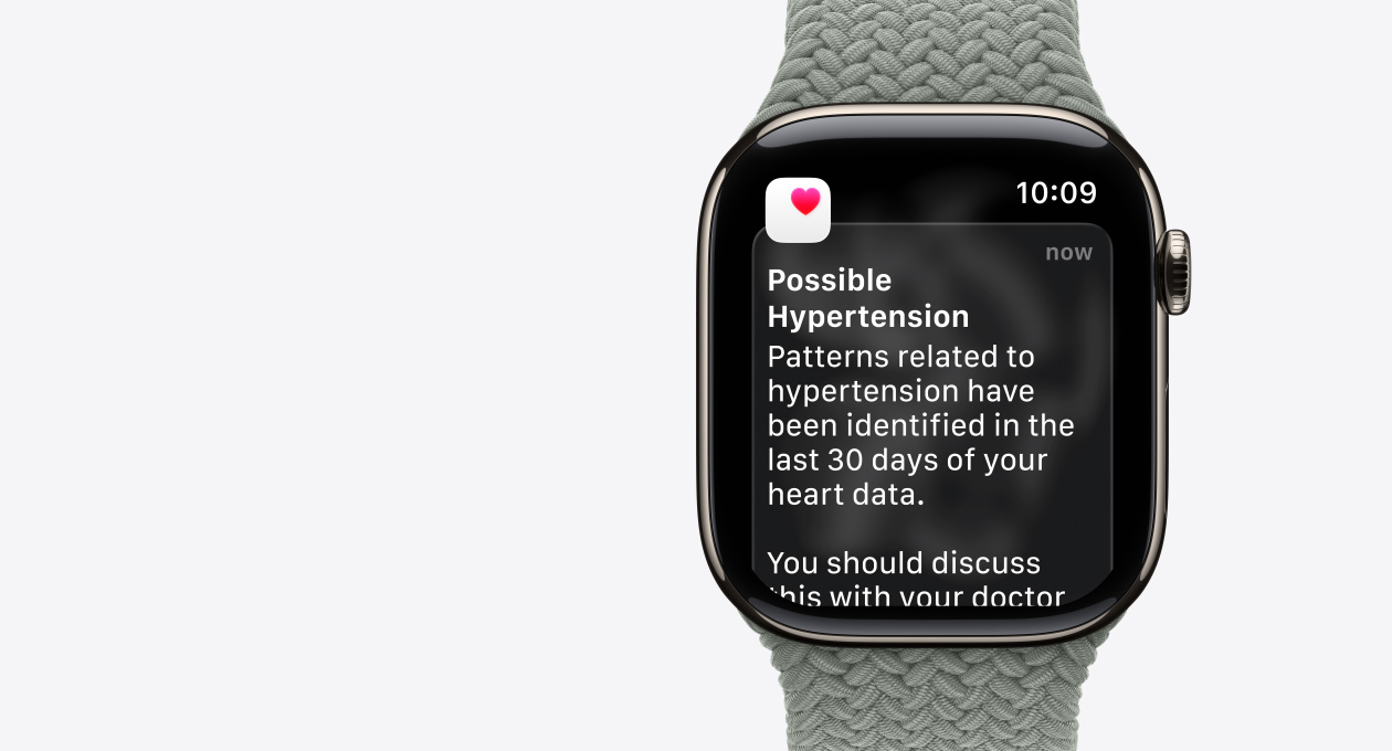 Apple Watch Series 11, culoare Natural, carcasă din titan, notificare de posibilă hipertensiune, inimă roz într-o casetă albă, partea laterală dreaptă exterioară, Digital Crown, curea, brățară împletită Solo Verde/Gri