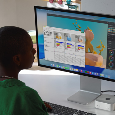 Employee sits and works on an Excel spreadsheet titled 'Q4 Sales Tracker' on iMac and Mac Mini. Behind the Excel spreadsheet is a Pixelmator Pro window and the macOS Tahoe background.