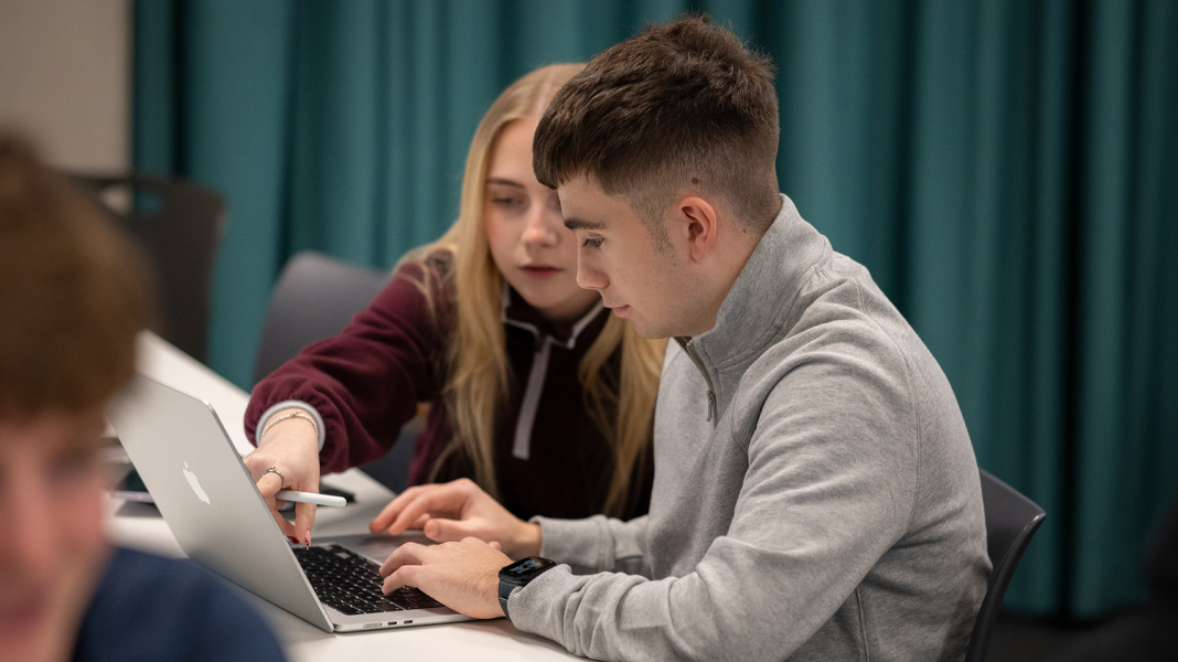 To medstuderende samarbejder på en MacBook. Hun peger på skærmen, mens han skriver