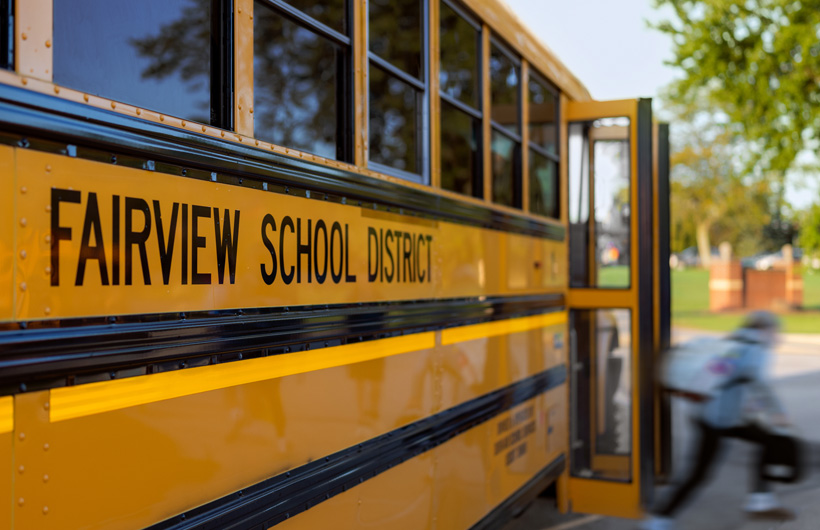 Et nærbillede af siden på en skolebus fra Fairview School District, mens et barn går ud af bussen.