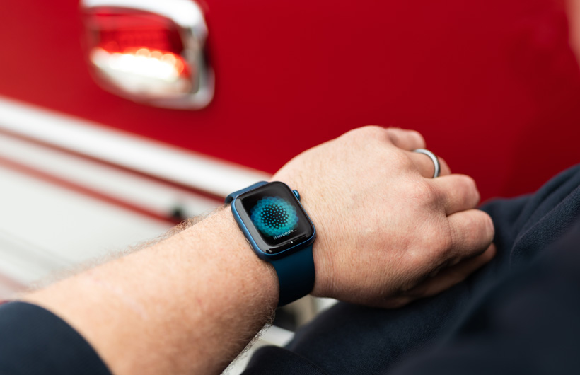 Braço com um Apple Watch que apresenta a mensagem "Inspire agora" e um camião de bombeiros por perto