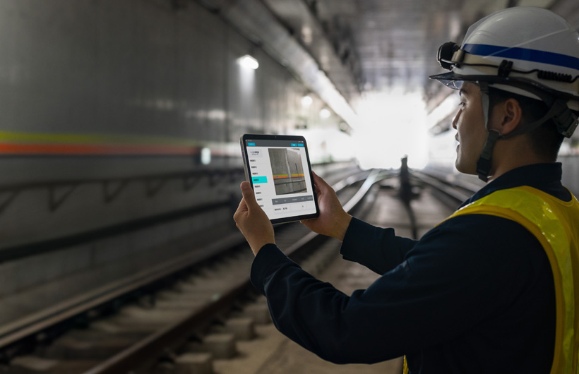 A maintenance worker in the tunnels of Tokyo Metro holds up an iPad to capture an image of the tracks while his colleague watches.