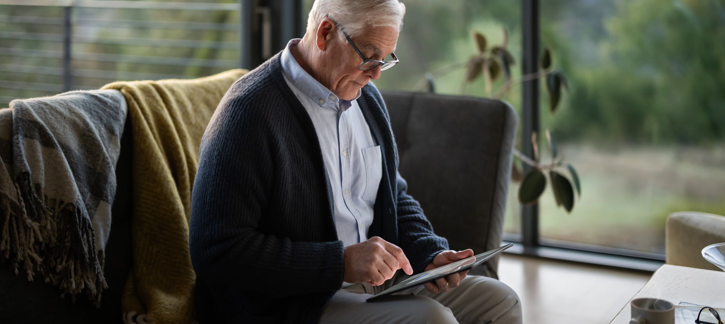 Ein älterer Mann sitzt auf einer Couch und schaut auf ein iPad.