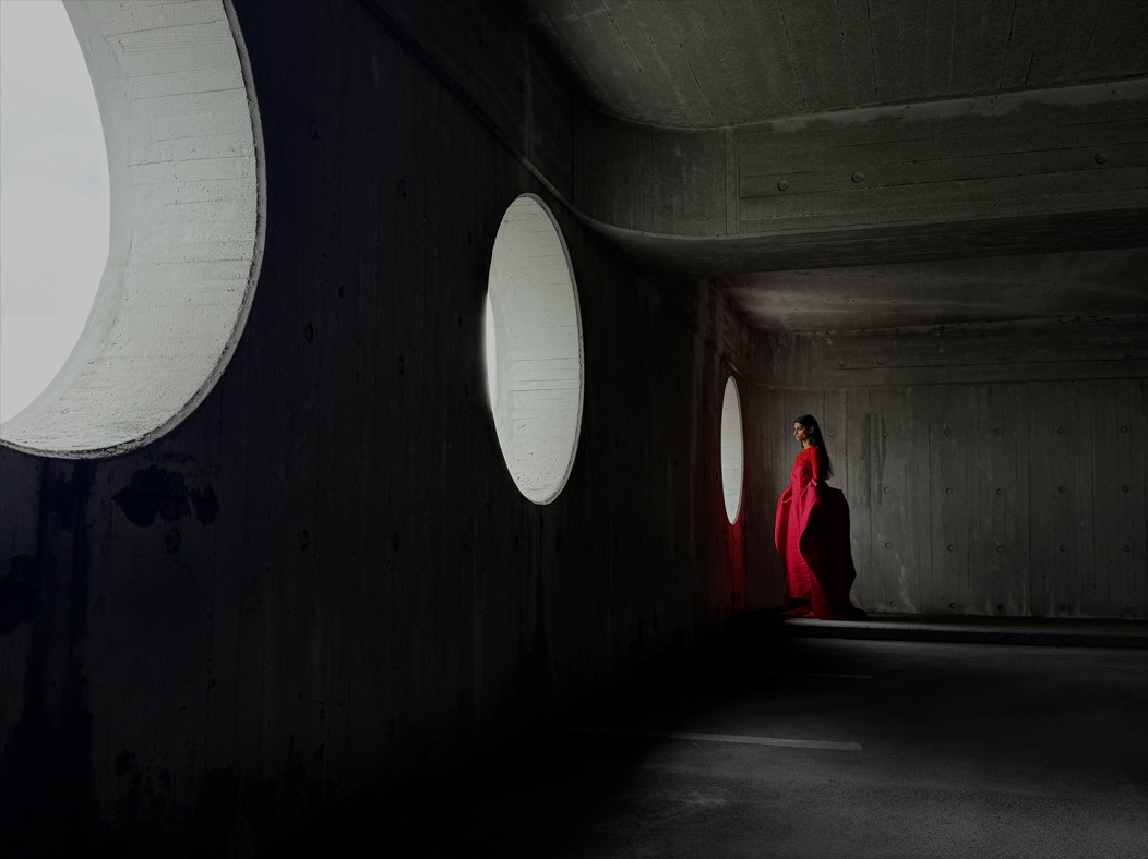 A woman wearing a long red dress stands in an empty room being photographed. The Photo app toggles through the focal lengths to demonstrate the capabilities of the pro camera system, showcasing: 35 mm