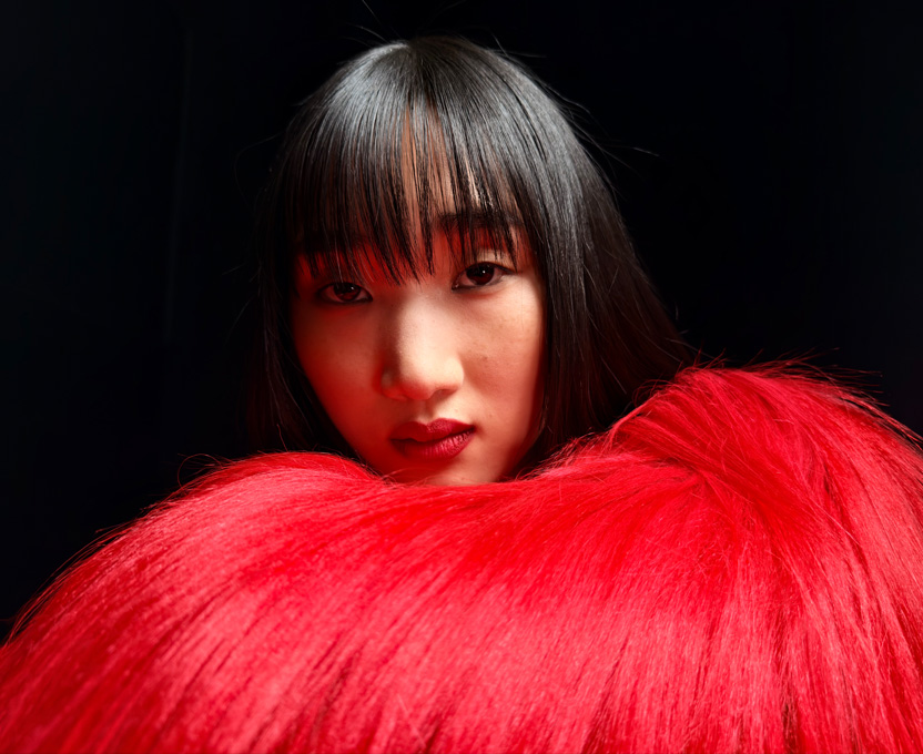 A close-up of a woman wearing a bright red feather top demonstrates the super-high-resolution photographic capabilities of iPhone 17 Pro
